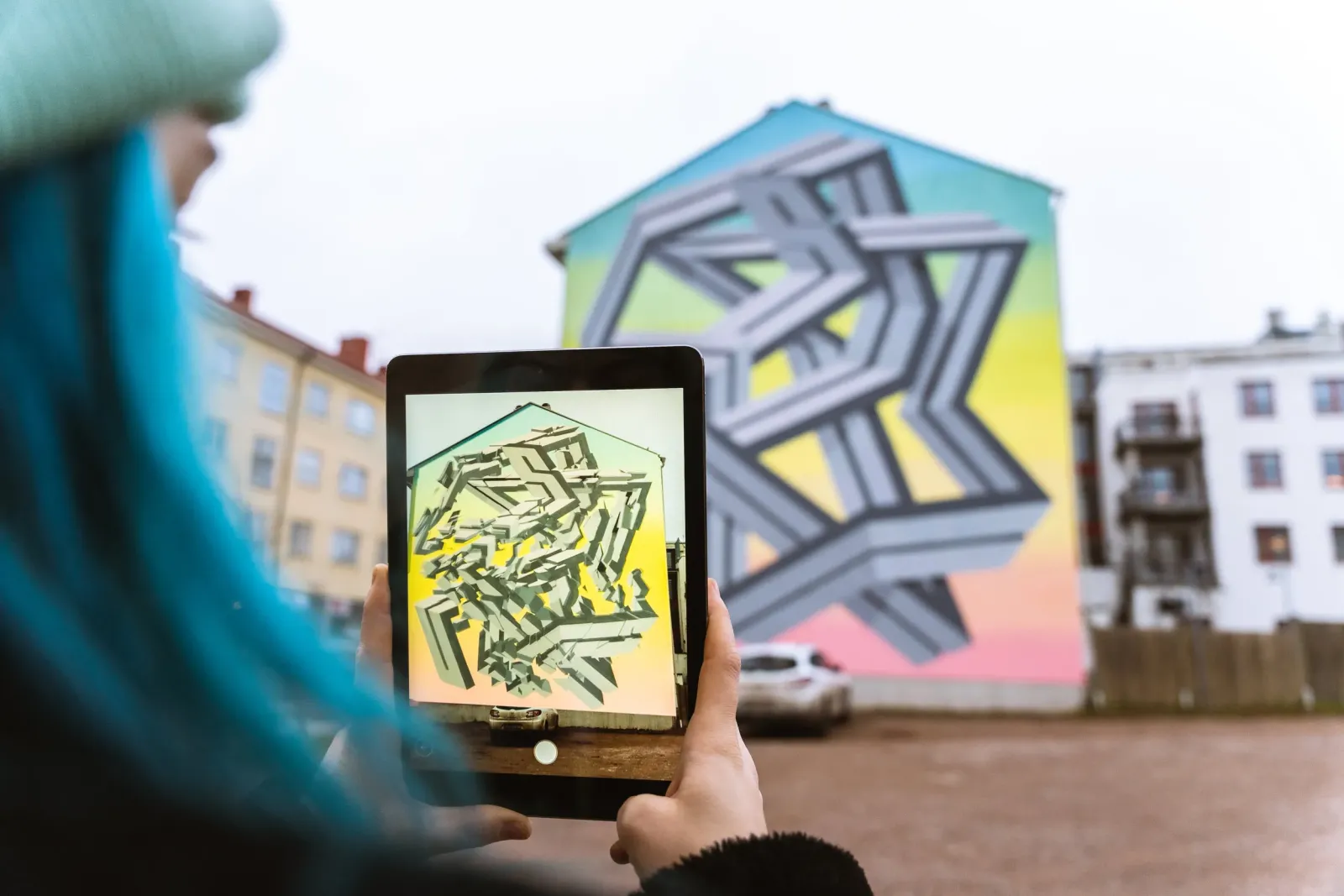 A tablet held up to a geometric street mural, showing the artwork lifting off the wall in 3D — an EyeJack Creator WebAR image target experience